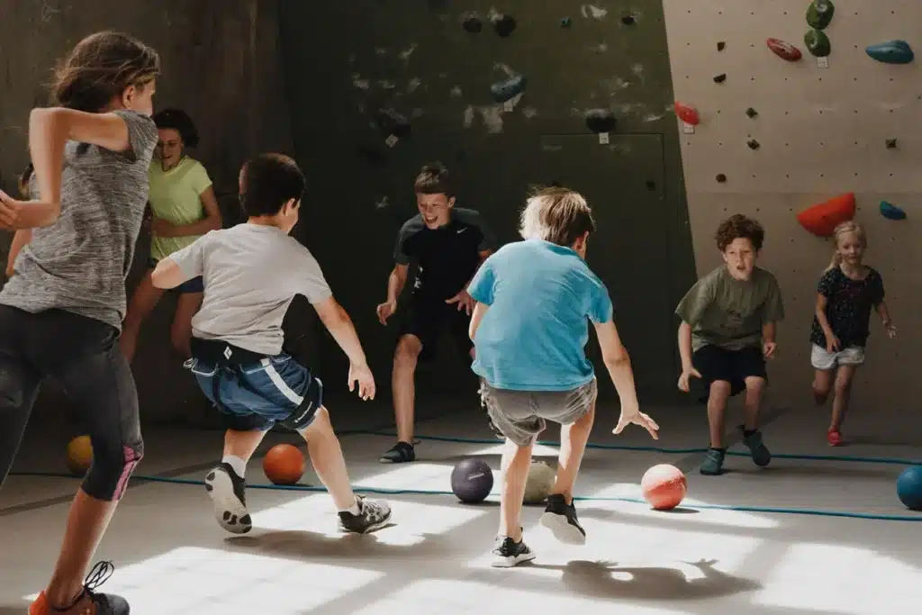 Children run to pick up dodgeballs in a climbing gym.